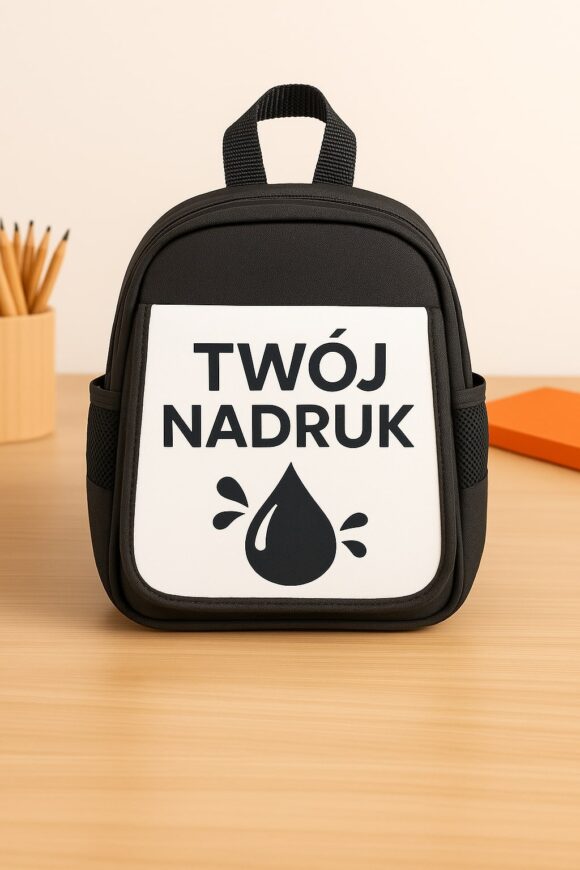 Czarny plecak dziecięcy z możliwością nadruku własnej grafiki – widok na klapkę z napisem „Twój nadruk” i kroplą, ustawiony na biurku w dziecięcym wnętrzu