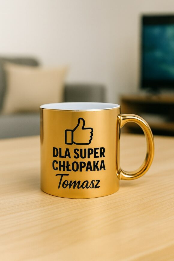 Złoty kubek personalizowany z napisem „Dla super chłopaka Tomasz” i grafiką kciuka, ustawiony na drewnianym stole w salonie.