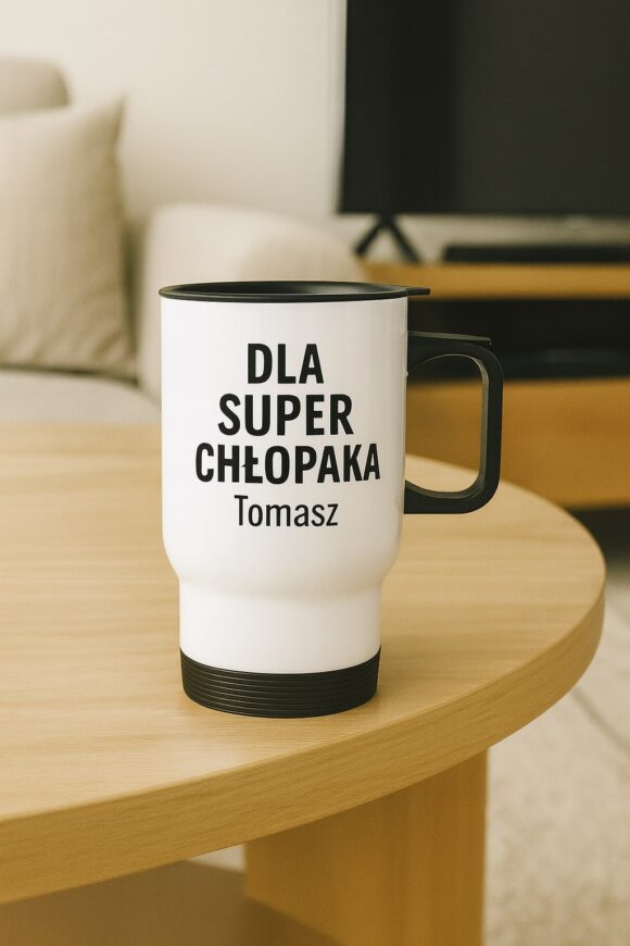 Kubek termiczny biały z czarnym uchwytem i napisem „Dla super chłopaka Tomasz” stojący na drewnianym stoliku w salonie.
